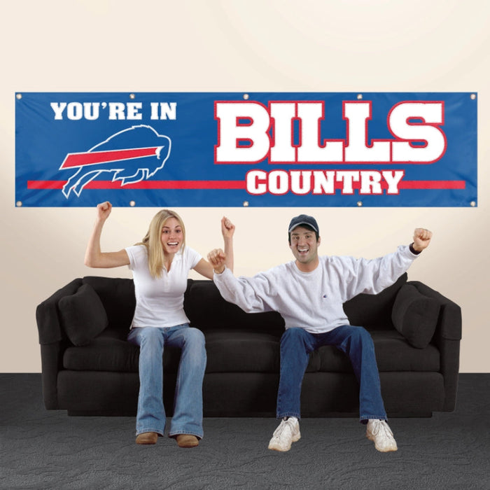 Two people sitting on a couch with a 'You're in Bills Country' banner in the background