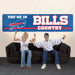 Two people sitting on a couch with a 'You're in Bills Country' banner in the background