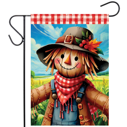 Garden flag with a scarecrow design featuring a checkered scarf and hat, against a scenic background.