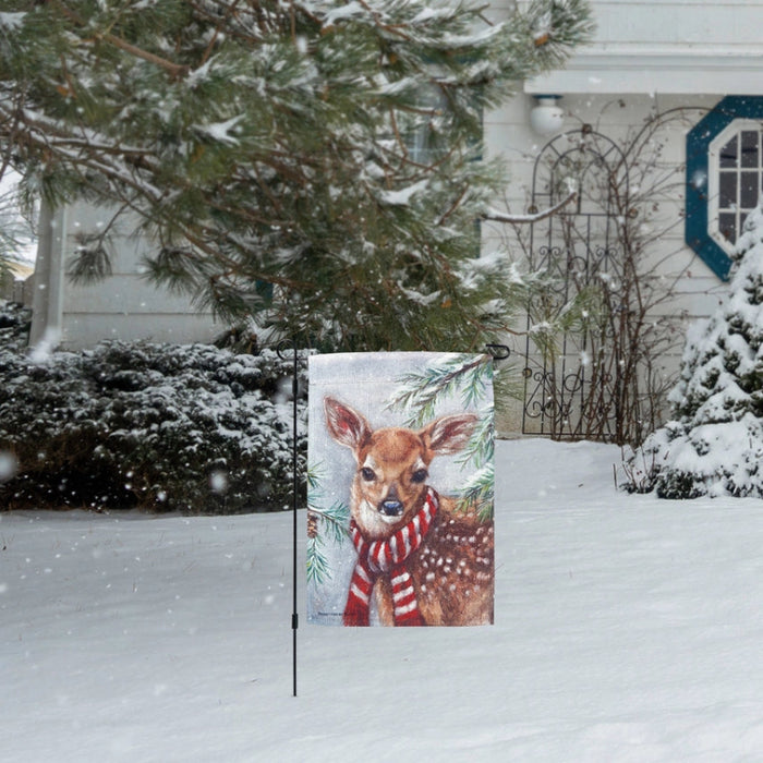Garden flag with a deer wearing a red and white striped scarf against a snowy background with pine trees