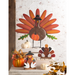 Decorative Thanksgiving turkey figures with pumpkins and leaves on a white brick wall background.