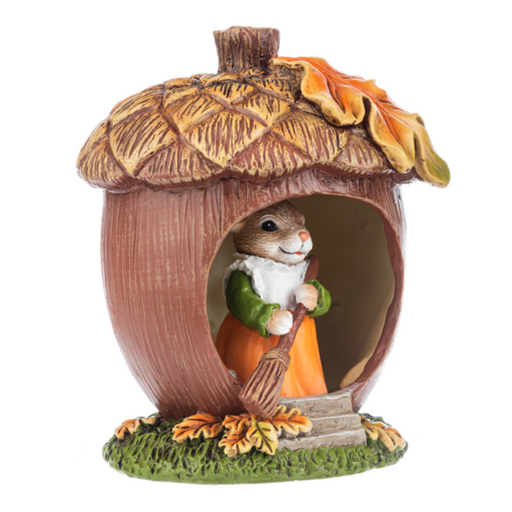 Decorative figurine of a mouse in an acorn house with autumn leaves and sweeping with a broom