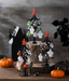 Halloween-themed decorative tree with ornaments on a wooden base, surrounded by pumpkins.