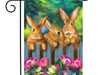 three bunnies behind a fence on a flag with colorful flowers in the front