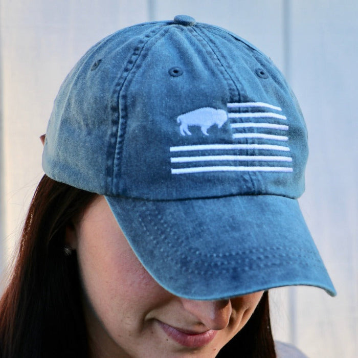 WOMAN WEARING THE BLUE VERSION OF THE HAT WITH A BUFFALO IN THE FLAG CANTON AREA AND STRIPES. EMBROIDERED