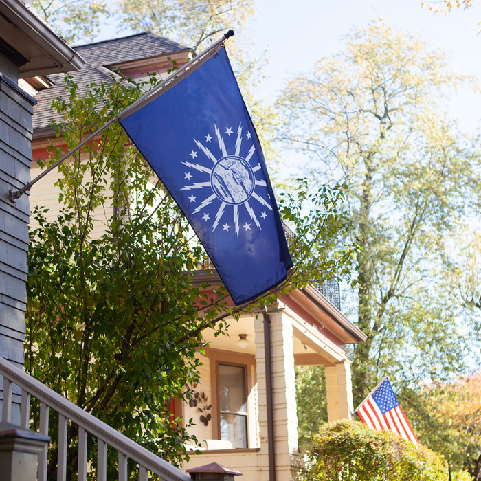 BLUE FLAG WITH A SHORE AND LIGHTHOUSE IN THE CENTER WITH LIGHTNING BOLTS AROUND THE CENTER ON A POLE OFF THE HOUSE