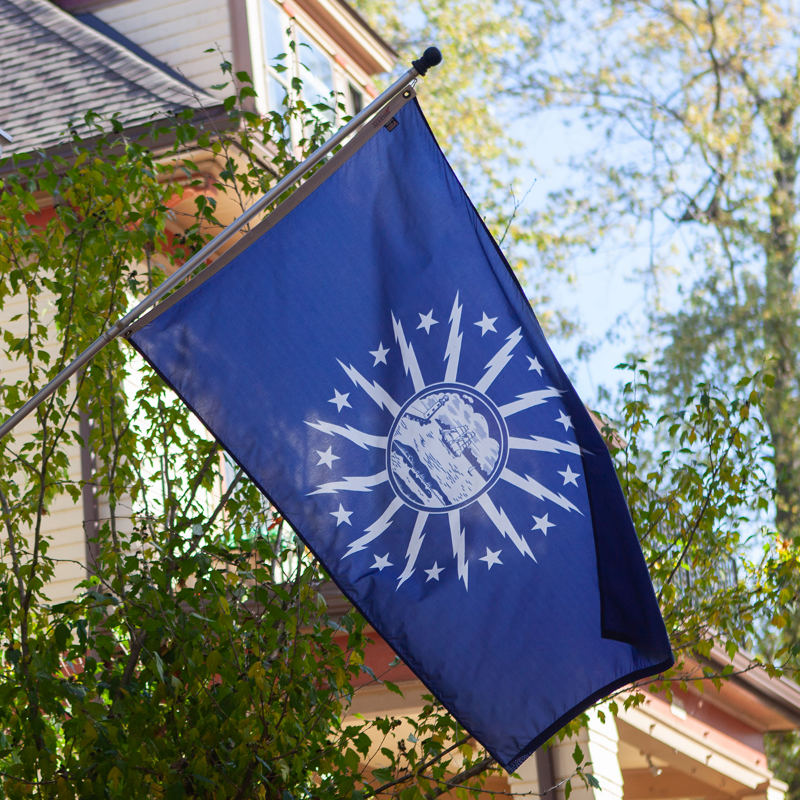 BLUE FLAG WITH A SHORE AND LIGHTHOUSE IN THE CENTER WITH LIGHTNING BOLTS AROUND THE CENTER ON A POLE